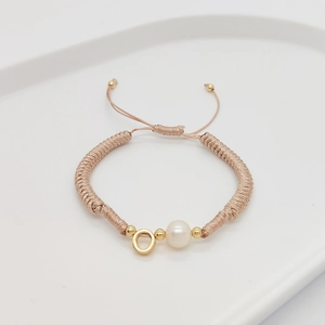 Close-up of handmade braided letter bracelet with white pearl and gold beads