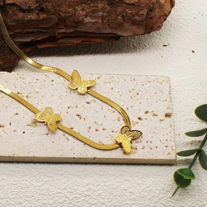Detail of a golden flat snake chain necklace featuring three textured butterfly charms