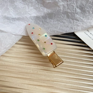 Close-up of cream acrylic hair clip with colorful rhinestones and gold metal base