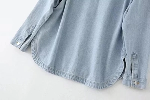 Detailed close-up of light blue denim shirt jacket featuring curved hem and metal cuff buttons
