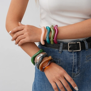 Close-up of stacked colorful acrylic wavy bangles in pink, blue and green on model arm