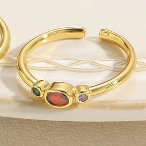 Macro detail of gold open ring with red oval stone and green and purple side gems