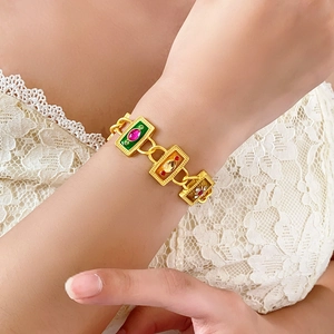 Close-up of vintage gold bracelet with colorful enamel flower charms on woman's wrist