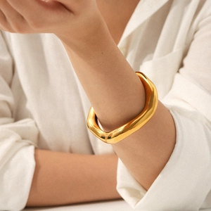 Irregular chunky gold wave cuff bracelet in stainless steel shown on model wrist
