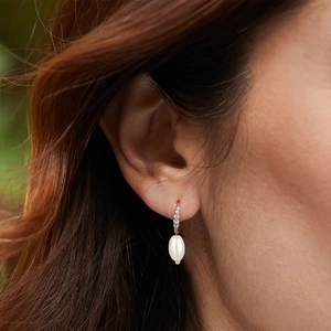 Macro detail of elegant gold pearl drop earring with zircon diamonds on model ear
