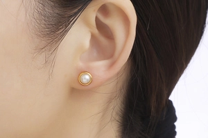 Close-up of minimalist gold rimmed pearl stud earring worn on a model's ear