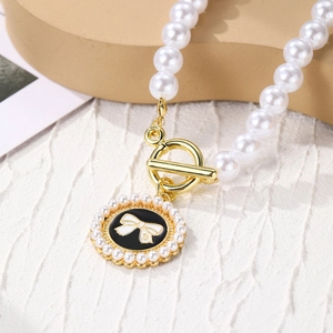 Detailed macro view of layered pearl necklace featuring a black enamel pendant with bow and number 5