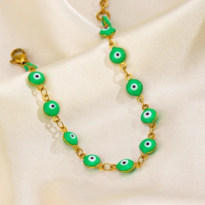 Golden stainless steel chain bracelet with green evil eye charms on silk background