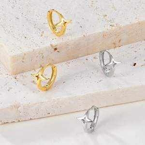 Close-up of gold and silver four-pointed star hoop earrings on a stone display base