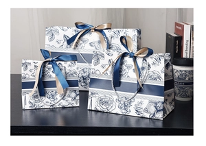 Three sizes of floral paper gift bags with blue ribbons on a wooden desk setup