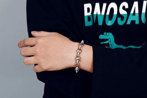 Close-up of a silver stainless steel O-chain bracelet on a model wrist against grey wall