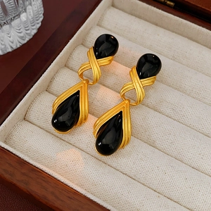 Detailansicht goldener Vintage-Knotenohrringe mit schwarzen Harztropfen auf beigem Samt