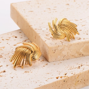 Golden irregular spiral earrings with textured wheat ear pattern on beige stone pedestal
