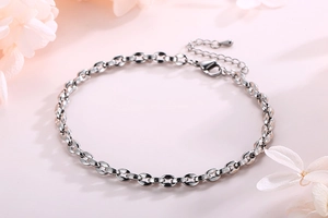Detail einer silbernen Edelstahl-Fußkette mit Karabinerverschluss auf rosa floralem Grund