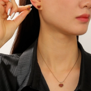 Close-up of model wearing gold heart earrings and necklace set with red inlay