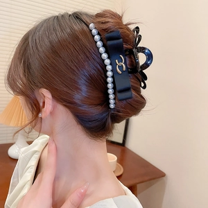 Detail shot of a black acrylic claw clip with pearls and ribbon on styled hair
