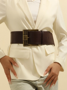 Close-up of a dark brown vintage leather belt with a bronze metal buckle on a beige blazer