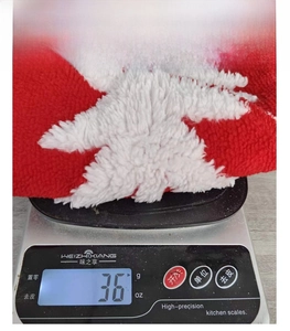 Detail showing the lightweight 36g red and white plush Christmas decoration on a digital scale