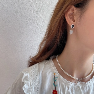 Detail view of black teardrop gemstone tassel earrings with white pearl necklace