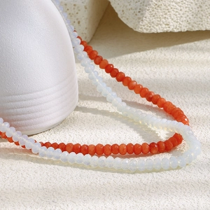 Close-up of double-layer necklace with orange and white beads on a textured surface