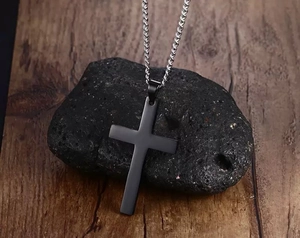 Detail of a black stainless steel cross pendant on a silver chain over a dark stone