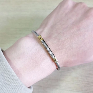 Close-up of a silver twisted steel cable bracelet with gold bar detail on the wrist