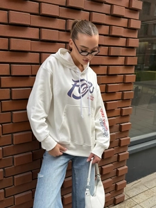 Outdoor street style shot of white hoodie showing front graphic and sleeve print detail