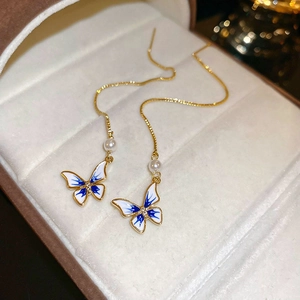 Détail macro de boucles d'oreilles papillon bleu et blanc avec perle dorée