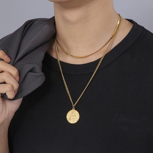 Close-up of layered gold snake chain and religious medallion pendant on black t-shirt