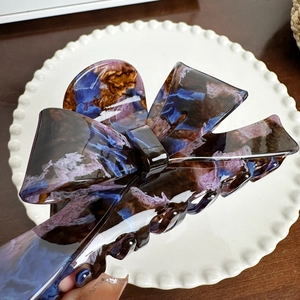 Large acetate bow hair claw clip with purple marble texture on a white plate