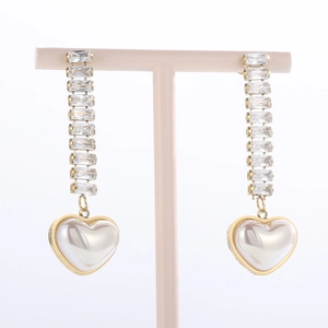 Close-up of long gold heart pearl earrings with sparkling crystal accents on a pink stand