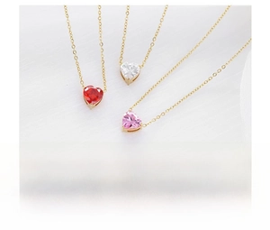 Primer plano de tres collares con piedras de corazón en rojo, rosa y blanco sobre oro fino