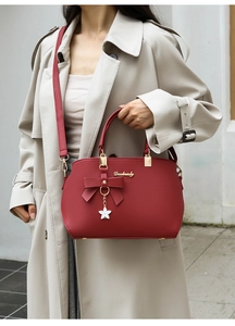 Close-up of red tote bag with bow detail and star pendant worn with a beige trench coat