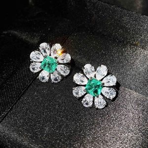 Macro shot of flower-shaped stud earrings with emerald-cut green stone and white petals