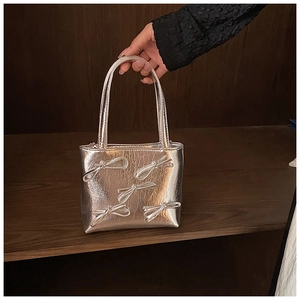 Detail of silver handbag featuring 3D bow decorations and a metallic finish surface