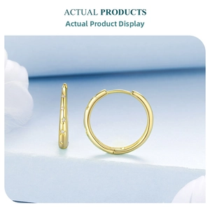 Macro shot of gold star-embossed hoop earrings on an elegant light blue display surface