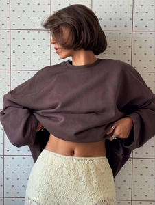 Oversize brown crewneck sweatshirt styled with white lace skirt on a model in profile