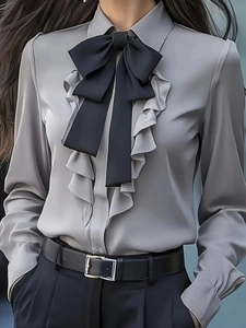 Detail of grey satin shirt featuring layered ruffles and a black ribbon bow tie