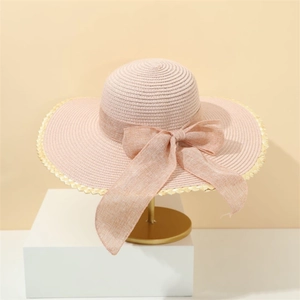 Detail of elegant pink straw sun hat with large bow and golden wavy brim texture