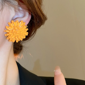 Macro shot of orange beaded flower stud earrings worn by a model on a beige wall