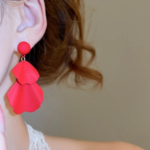 Close-up of red petal tassel earrings worn with a matte finish and layered floral design