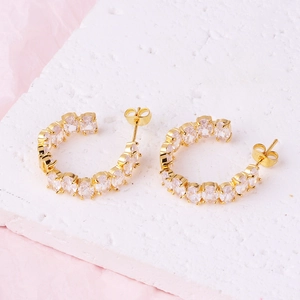 Elegant gold-plated C-shaped hoop earrings with clear zircon stones on a white stone base