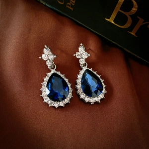 Macro detail of silver halo earrings with teardrop blue stones on brown silk background