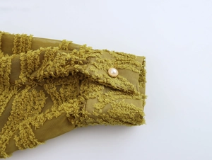 Detail of moss green textured shirt cuff with pearl button and gold trim accent