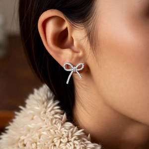 Detailed close-up of a silver bow ear cuff with sparkling zircon stones on a model's ear