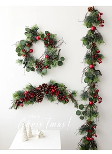Detail of Christmas garland with red berries and pine cones on a white wall