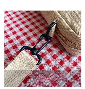 Detail shot of matte black metal hook and thick woven strap on beige canvas mini bag