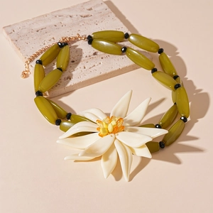 Macro detail of a resin white flower pendant on an olive green beaded choker necklace