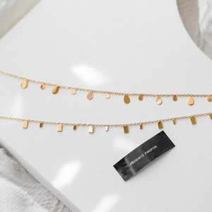 Layered gold titanium necklaces with droplet and bar pendants on a white display