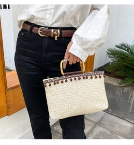 Detail of straw woven tote bag featuring brown tassel fringe and square metal handle